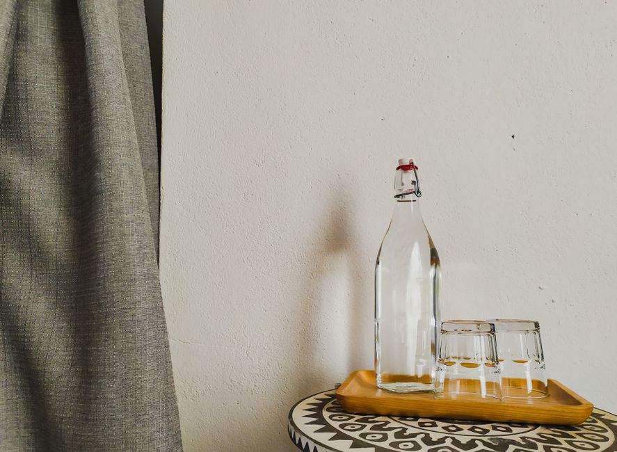 Minimalist composition of a glass bottle and glasses on a wooden tray indoors.