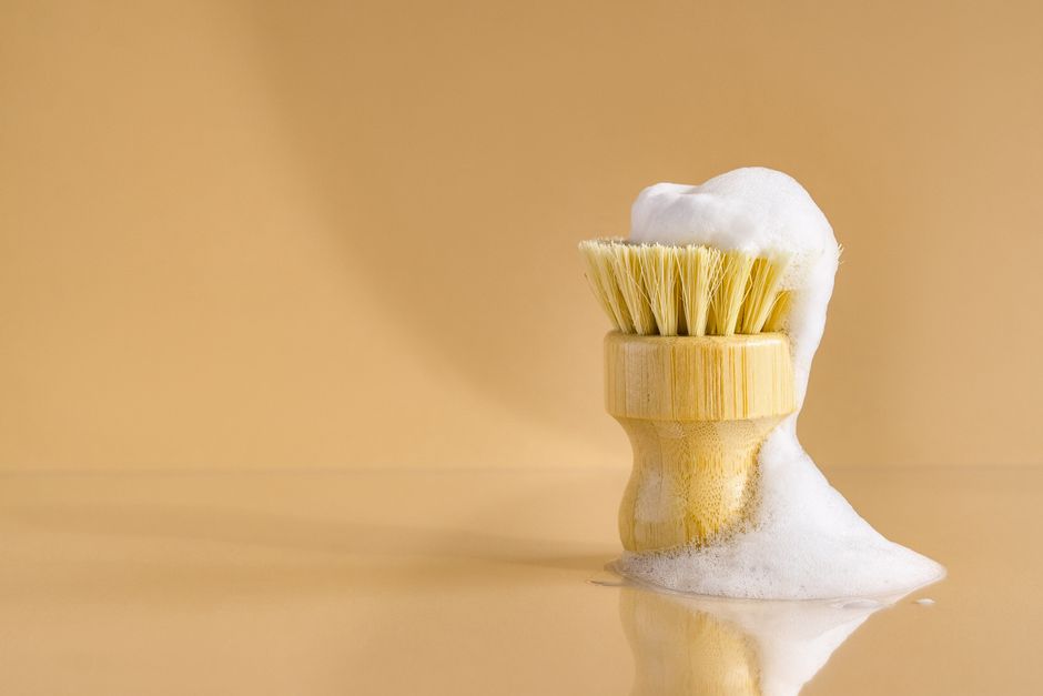 Eco-friendly bamboo brush with bubbly foam on a minimal beige background, highlighting clean living and sustainability.